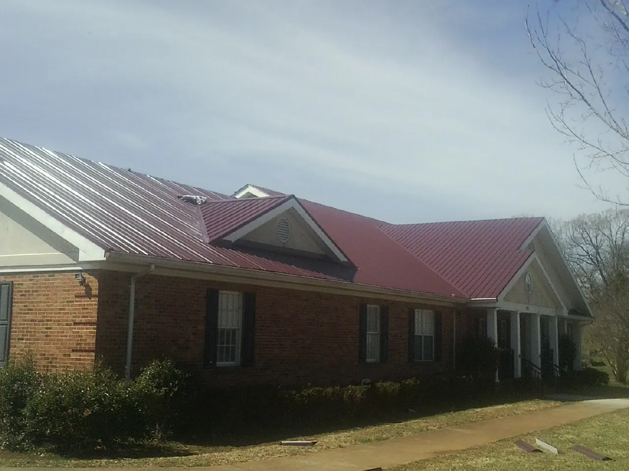 Red metal roof with gabled entries on a long brick building, from a Hail Damage Roof Repair job in Blackfoot