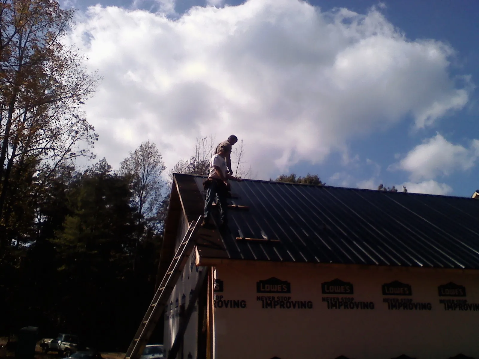 Roofer fastening dark metal panels high against a cloudy sky, from a Roof Inspection job in Blackfoot