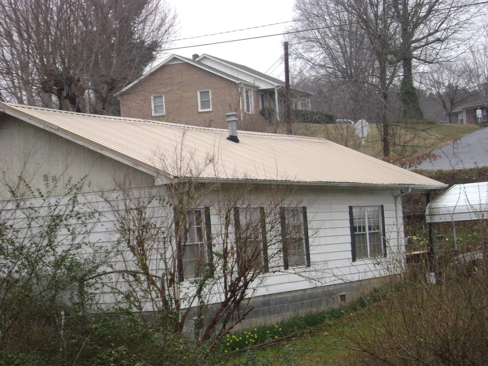 Tan metal roof on a white sided house set into a hillside — Commercial Roofing by Roofing Brothers in Blackfoot