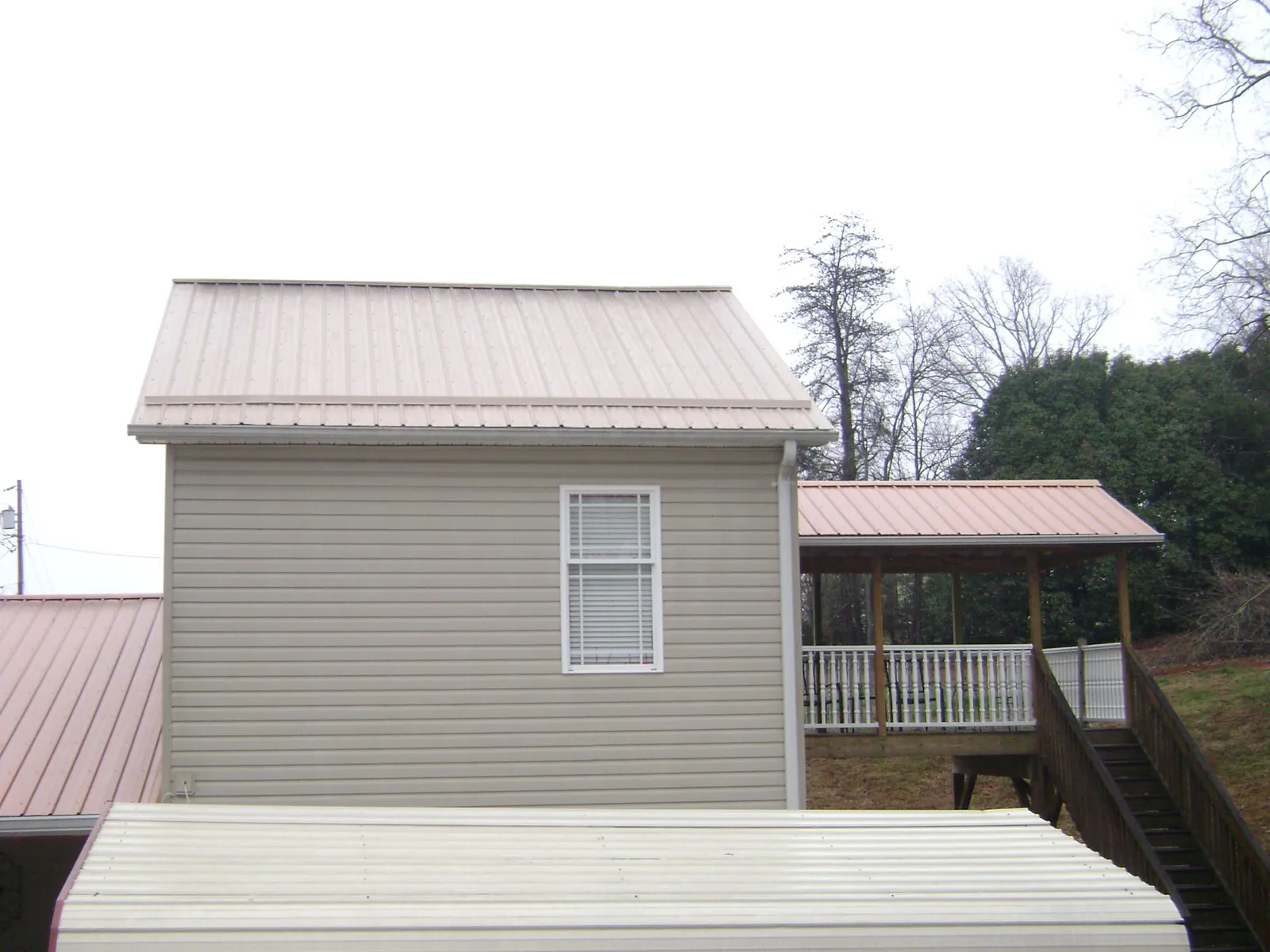 Tan metal roofs on a two story addition and attached porch, from a Roof Replacement job in Blackfoot